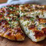 Golden-brown The Best Easy Garlic Naan Bread served warm alongside a rich curry with chopped cilantro garnish.