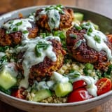 Crisp baked falafel sits atop a bed of fluffy quinoa in this wholesome salad bowl, drizzled with creamy garlic tahini sauce.