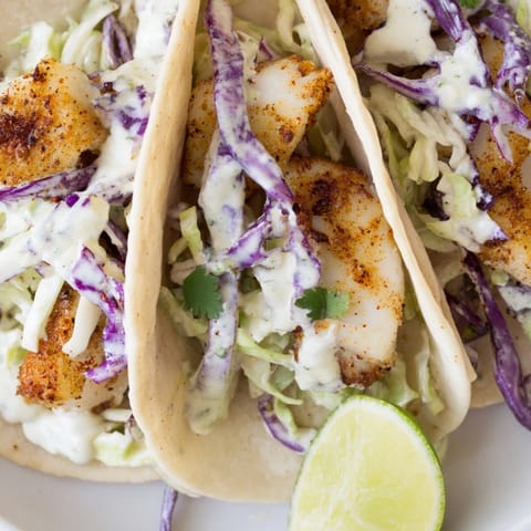 Soft tortillas hold perfectly seasoned, flaky fish tacos featuring a vibrant slaw and creamy sauce.