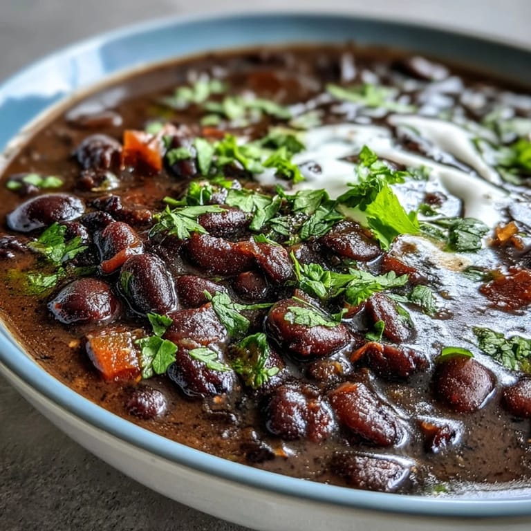 A steaming bowl of black bean soup with lime wedges and sour cream.