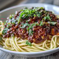 A bowl of hearty Lentil Bolognese sauce over spaghetti, garnished with fresh basil and vegan cheese.
