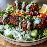 Crispy falafel balls rest on creamy hummus and greens in this vibrant falafel bowl, ready for a Mediterranean-inspired meal.